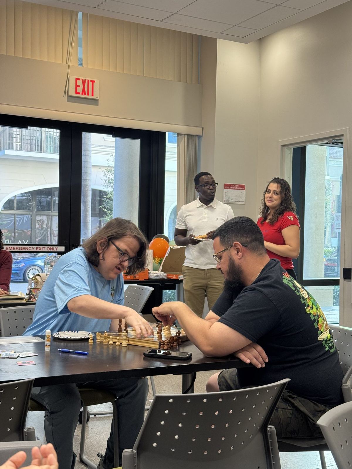 Two participants playing chess together at an ACES community session while staff assist nearby